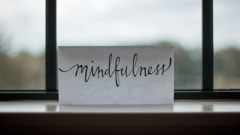 “Mindfulness” written in cursive on white paper on a windowsill