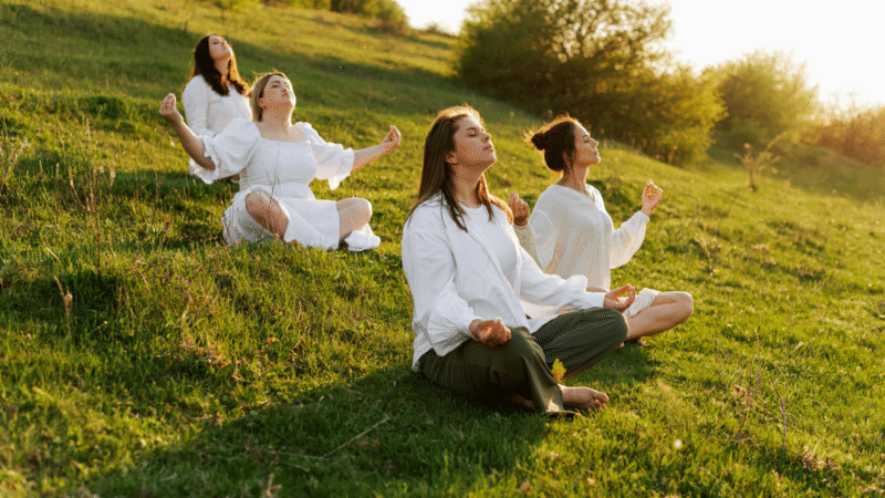 Group of women in white shirts, practicing guided meditation outdoors
